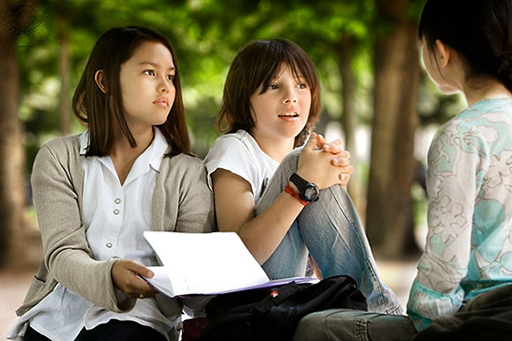 An image shows three teenage students sat outside, in discussion.