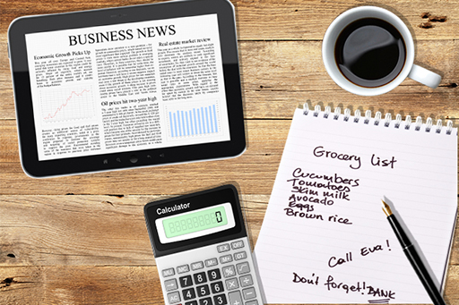 On a table is a mobile device displaying a newspaper article on business news, a calculator and a shopping list.