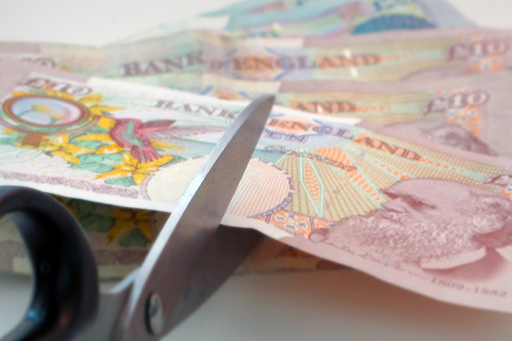 A £10 note is being cut in half by a pair of scissors.