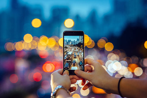 A photograph of someone holding up a smartphone, taking a picture of traffic.