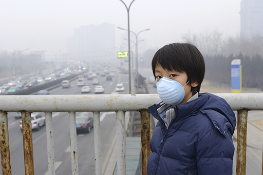 An image of a boy wearing a face mask, standing on a bridge over a motorway surrounded by smog.