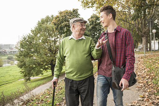 A photograph of an elderly man walking with a teenage boy through a park.