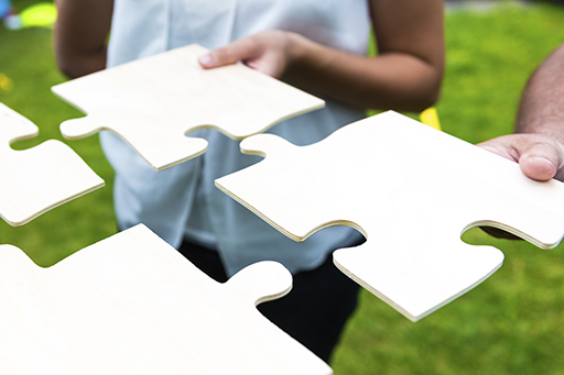 Image of two people holding large jigsaw puzzle pieces and preparing to slot them.