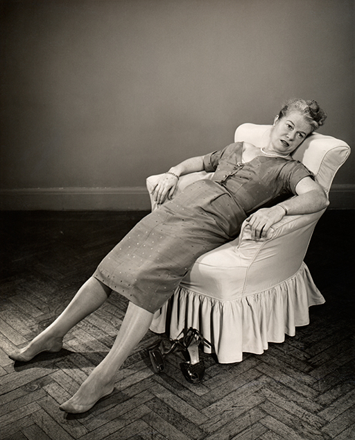 A black and white photo of a woman slouched in an armchair looking exhausted.