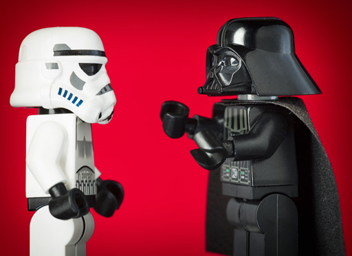 Lego mini figures of Darth Vader and a Stormtrooper facing each other against a red background.