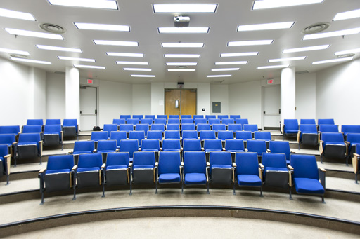 An empty lecture theatre with tiered blue seats and white walls.