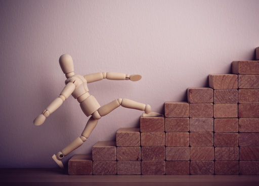 A wooden mannequin climbs up some wooden blocks arranged as stairs.