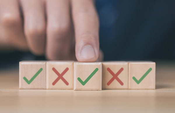 Hand placing a wooden block with a green check mark among a row of blocks displaying green tick marks and red X symbols, representing evaluation or selection.