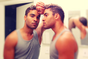 Photograph of a young man gazing at his reflection in a mirror