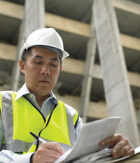 Man on a building site in a hard hat writing notes