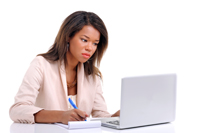 Photograph of a young black woman seated at a laptop with pen and paper in hand