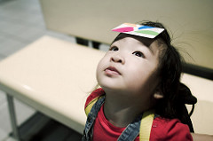 Little girl looking up very still and holding a piece of paper on her forehead