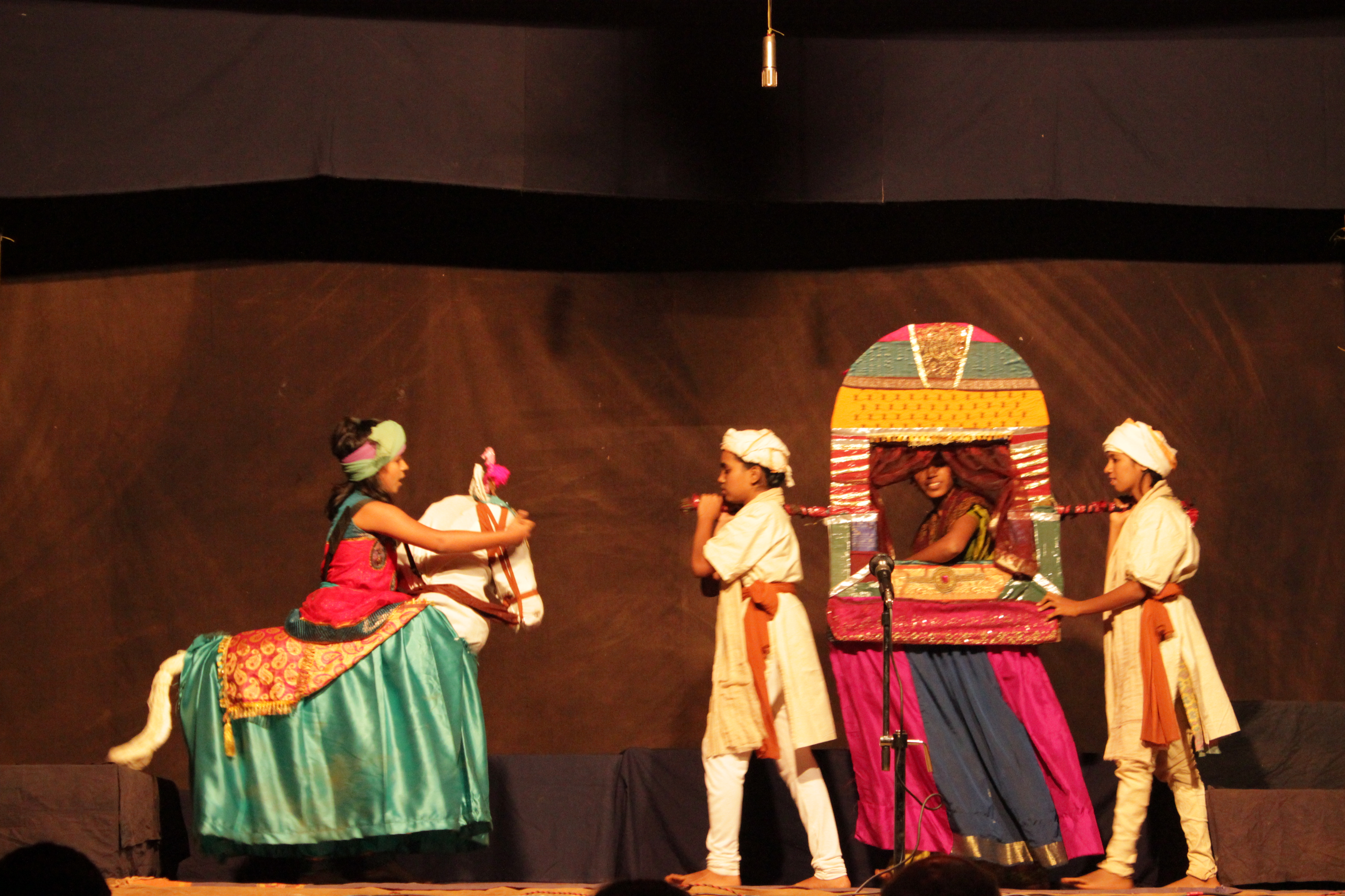 Child on the left inside puppet horse facing two children to the right carrying a third child in a carriage.