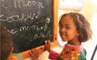 A young child writes on a blackboard with chalk.