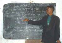 A male health worker giving a lecture stands in front of the blackboard.