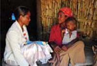 A health worker talks to a mother at her home. Her small child sits on her lap.
