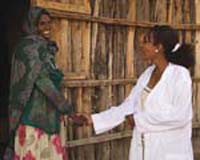 A health worker greets a woman outside her home.