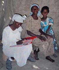 A healthcare worker taking notes as she sits talking with a woman and her child.