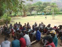 A large group of people are sitting around listening to a healthcare worker.