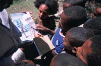 A group of children gather around to look at a picture about health issues.
