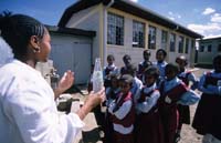 A healthcare worker gives a practical demonstration to school children outside their classroom.