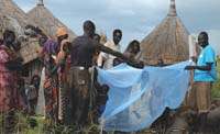 Members of the community are shown how to properly place the bed net over the bed.