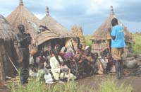 A family group are seated outside their home listening to a man talk about health issues.