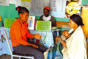 A health worker is talking to a mother. A baby lays asleep on the mothers lap.