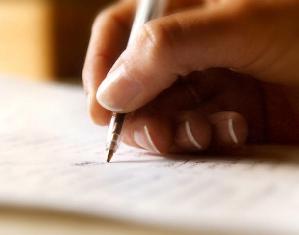 A persons hand holds a black biro while writing on a page.