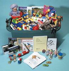 Cette photo montre une boîte contenant toutes sortes de jouets et de jeux, y compris des poupées, des figurines, des voitures miniatures et des livres. Ce sont des matériaux utilisés dans certains modules de l'ADOS.