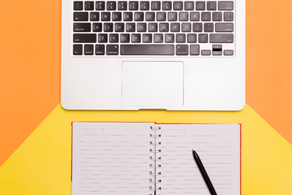 Photo of a computer and a notebook journal and pen