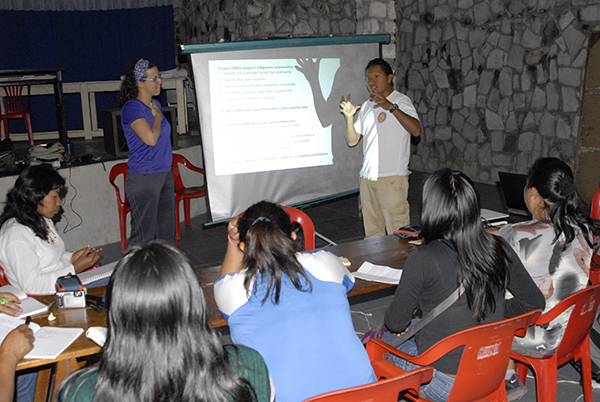 A picture of someone standing by a screen and facilitating a discussion with a group of people