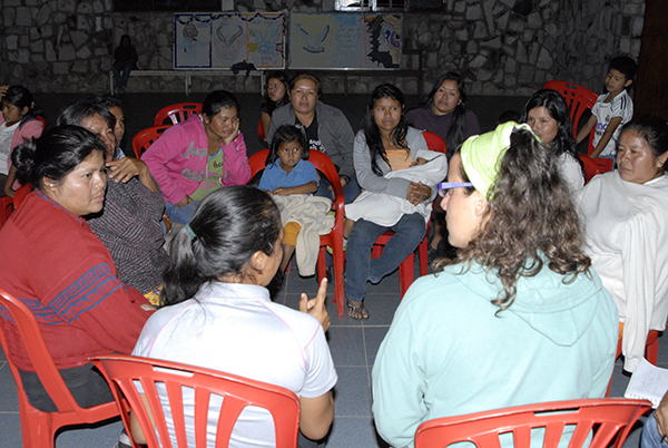 People of all ages and genders sat in a circle on chairs holding a community meeting
