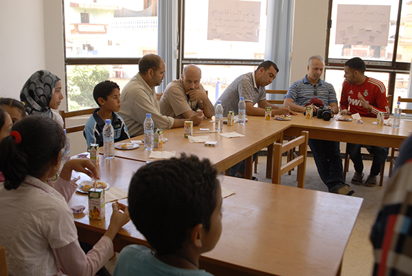 Photo of community members of all ages and genders sat around tables holding a meeting