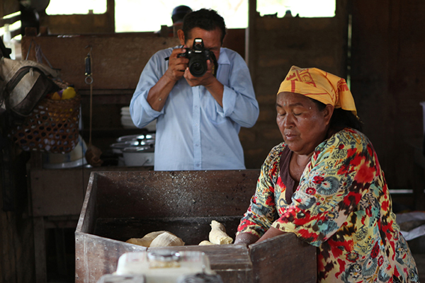 A person taking a photograph of someone grating cassava