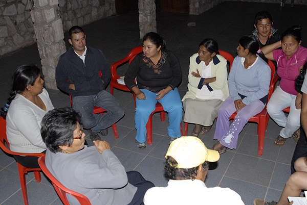 A photo of community members sat on red chairs in a circle discussing the results of environmental monitoring