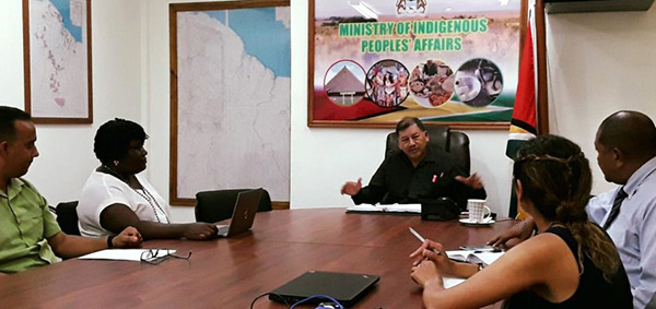 Photo of a group of people sat around a table meeting a Minister of the Guyanese Government