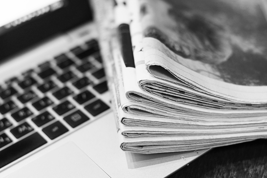 A black-and-white picture of a stack of newspapers covering an open laptop.
