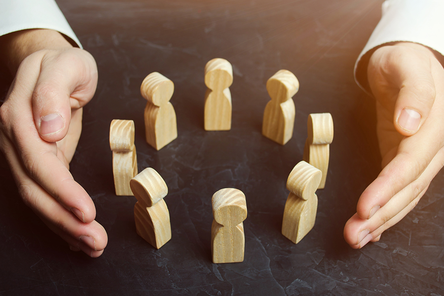 A pair of hands surrounding eight wooden figures arranged in a circle.