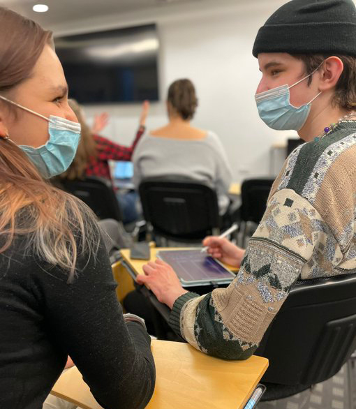 Dos estudiantes mirándose, sentados cada uno a su mesa.