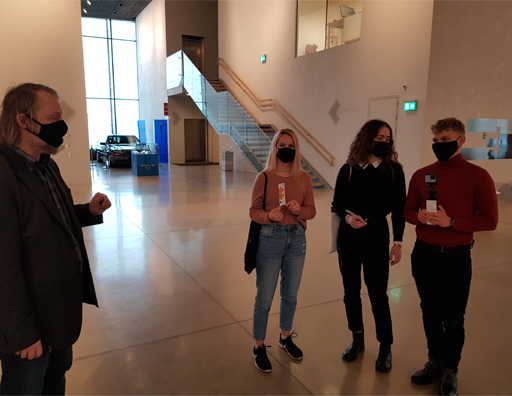 Een leraar in gesprek met drie studenten in een museum