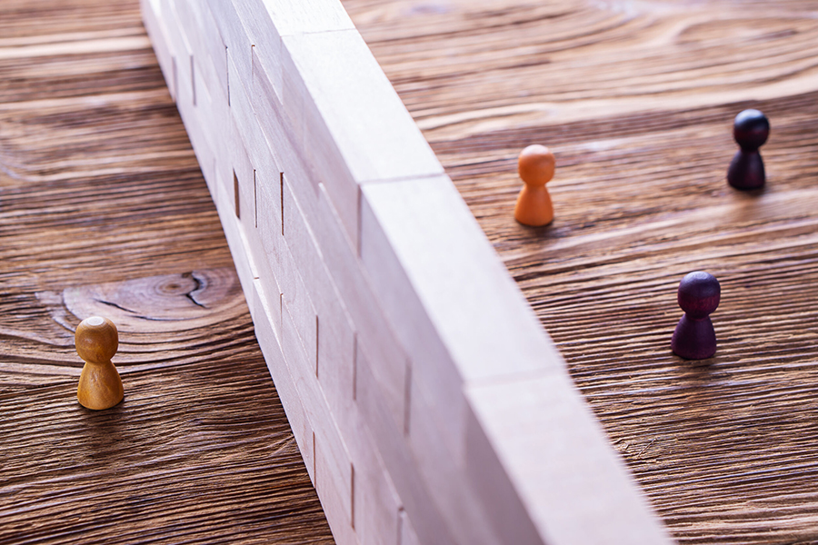 An image depicting wooden figures of people on either side of a wall.