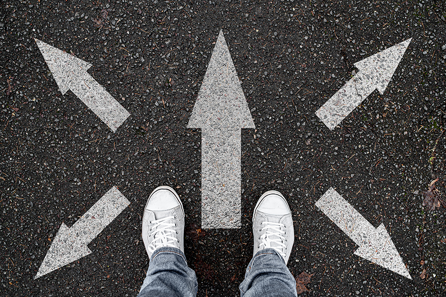 An illustration of a pair of human feet, in trainers and jeans, standing on a dark surface. A painted arrow is pointing straight ahead of the feet. To either side there are other arrows pointing in different directions.