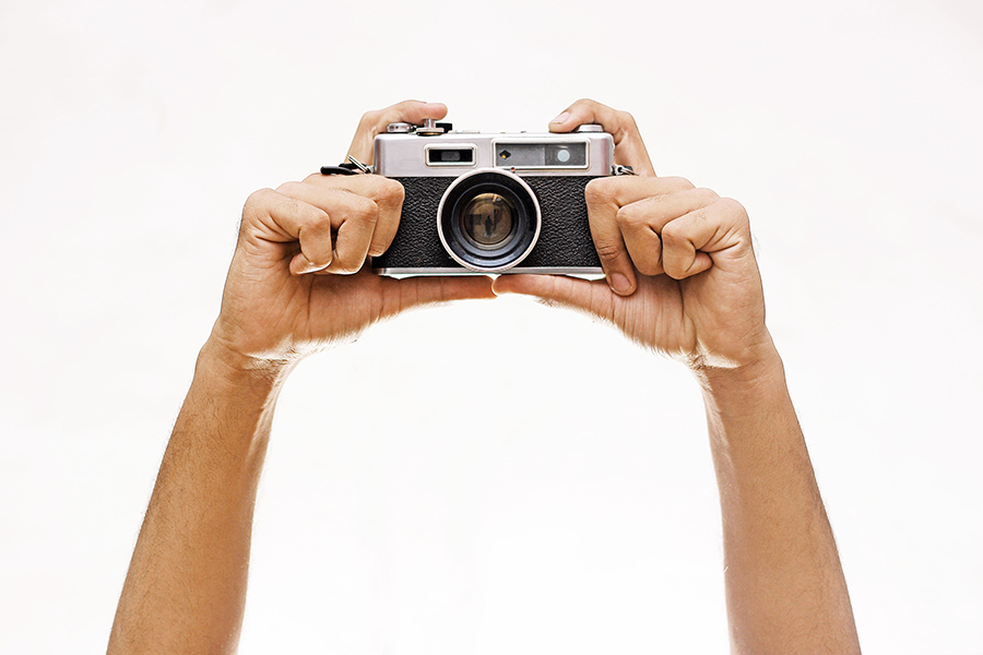 An image of someone holding a camera high above their head. Only the person’s arms and the camera are visible.