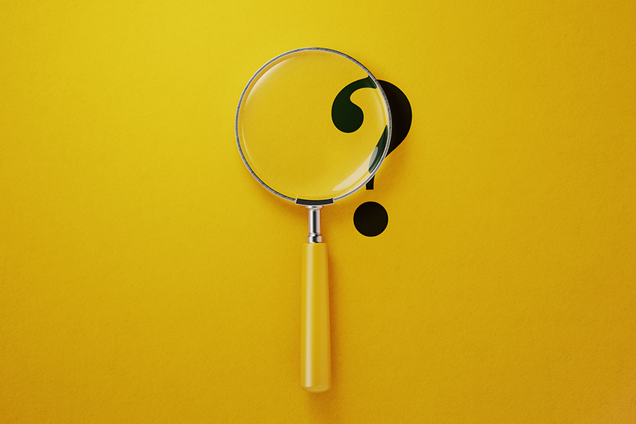 A decorative image depicting a flat surface with a question mark printed on it. A magnifying glass is laid partially over the question mark.