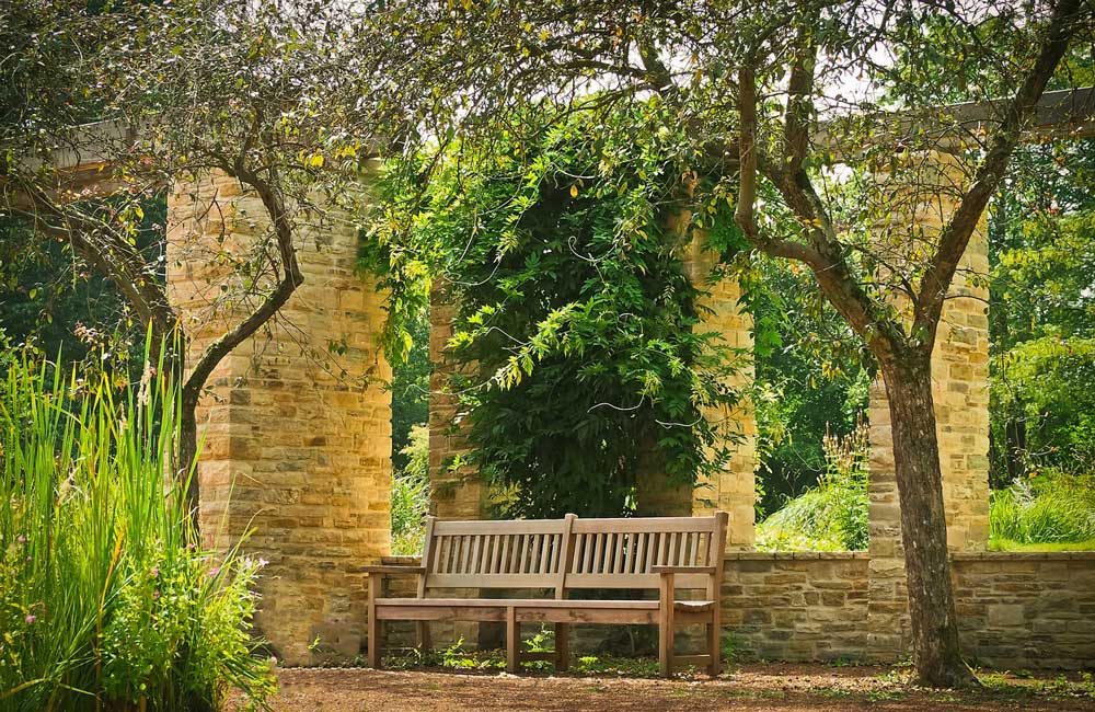 A wooden garden seat in an enclosed area of brickwork and planting