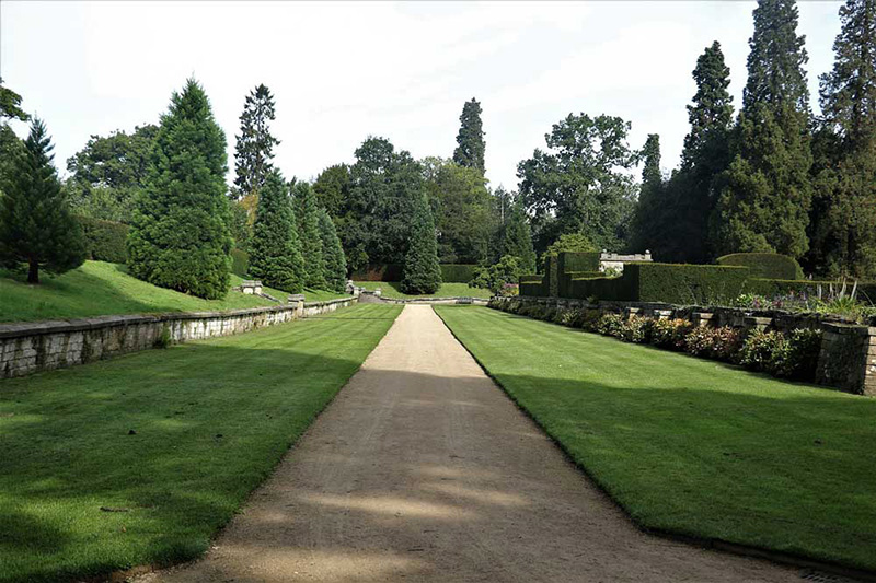 Neatly clipped lawns and trees bordering a straight pathway through a formal garden.