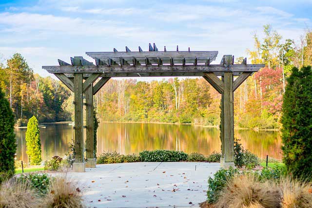 Japanese style wooden pergola standing in gardens next to water.