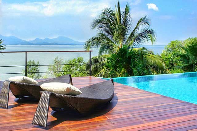 Sunloungers on wooden decking next to a pool with sea view.