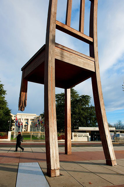 A sculpture of a giant wooden chair with one broken leg  in a public park
